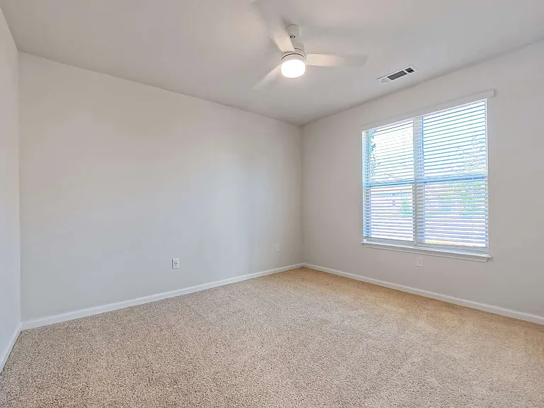 Bright and airy bedroom with plush carpet, large window offering natural light, and a modern ceiling fan.