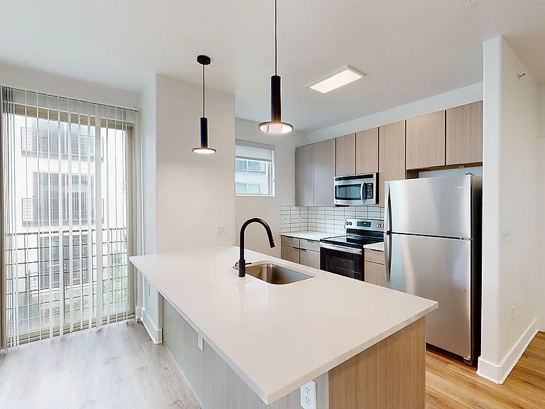 Apartment kitchen with stainless steel appliances, quartz countertops and wood-style flooring.