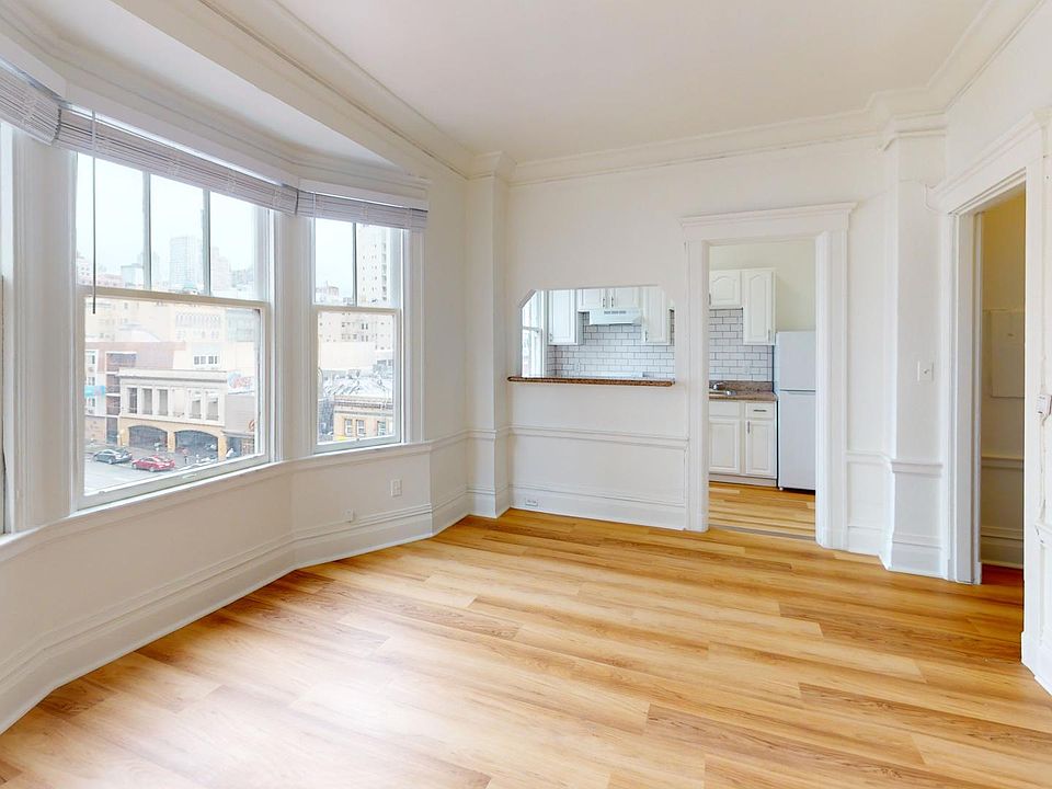 Sunlit room with a large window, wood-like flooring and a view of the kitchen