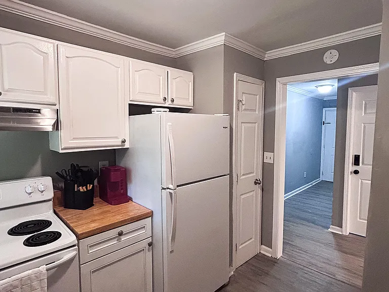 Efficient kitchen with ample white cabinetry, full-size refrigerator and range, and durable flooring with an open entry to th