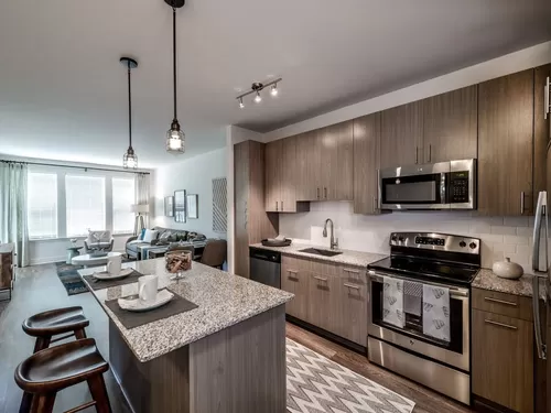 Open concept kitchen with brown cabinetry, granite countertops, kitchen island, stainless steel appliances, tile backsplash and hard surface flooring - Avalon Arundel Crossing