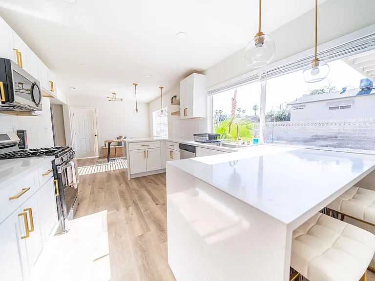 Updated kitchen with quartz counters, gas range, dishwasher, and a breakfast bar overlooking a large window.