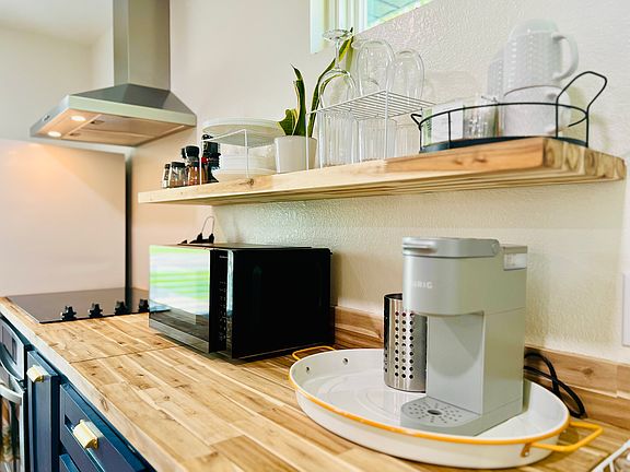 Stocked with cups/plates/bowls, spices, pot & pan, cooking & eating utensils, small blender, coffee maker, microwave and toaster.