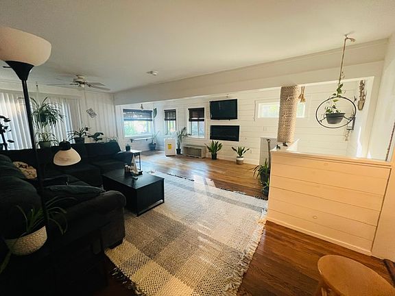Living room with lots of light, wrap around couch, tables, electric fireplace, TV, A/C, and lake view.