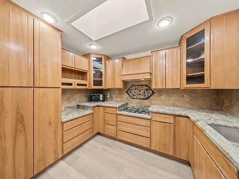 U-shaped kitchen with extensive wood cabinetry, generous counters, tiled backsplash, and a built-in gas cooktop plus sink.