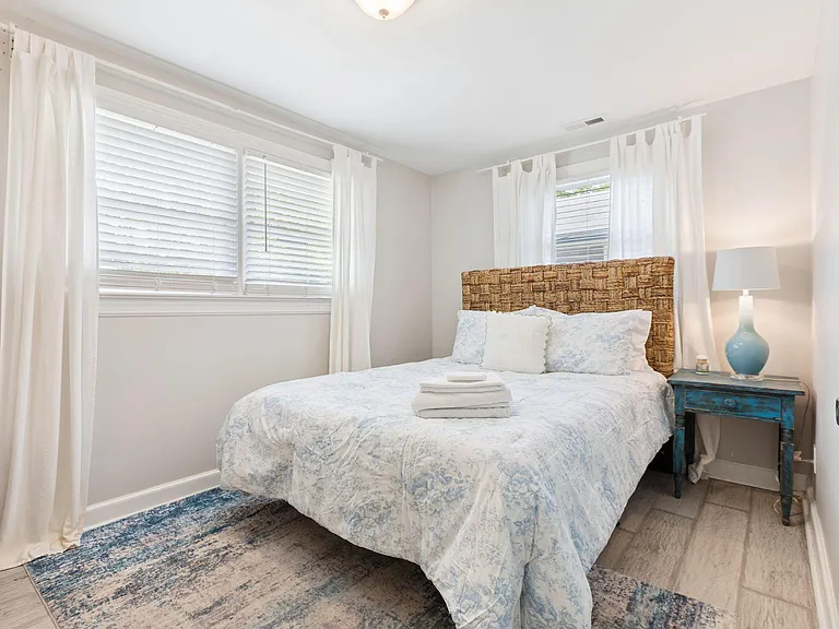 Inviting bedroom with a full bed, nightstand lighting, and dual windows with blinds and curtains for adjustable privacy.