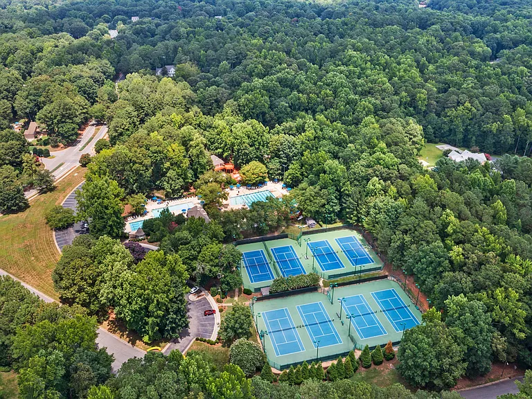 Community pool and tennis amenities surrounded by a beautiful wooded backdrop.