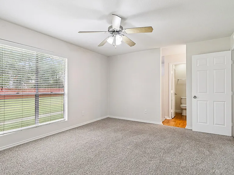 Bright and airy bedroom with plush carpeting, large window for natural light, ceiling fan, and attached bathroom. Bright and airy bedroom with plush carpeting, large window for natural light, ceiling fan, and attached bathroom.