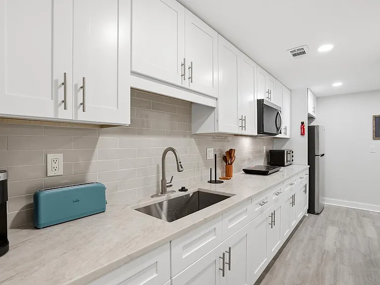 Galley kitchen with white shaker cabinets, subway-tile backsplash, and long counters plus stainless sink, microwave, and frid
