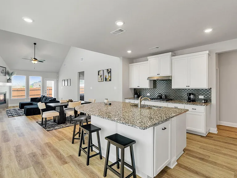 Open-concept kitchen featuring an island with granite countertop, white cabinetry, and a textured tile backsplash