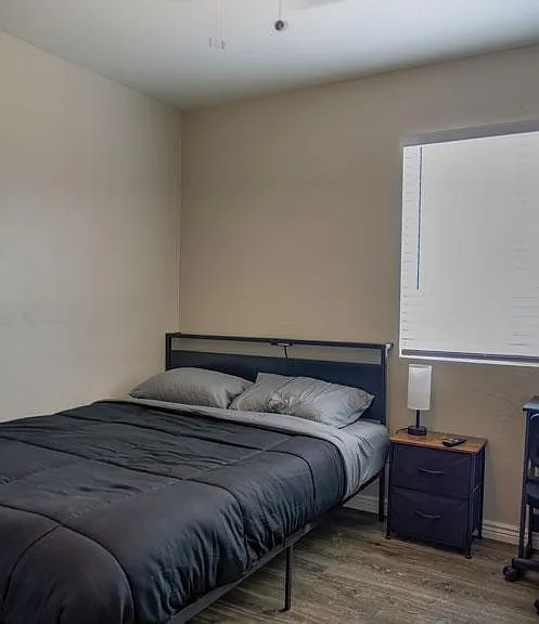Furnished bedroom with a full bed, nightstand, and desk, plus a window with blinds and ceiling fan lighting.
