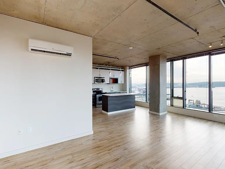 Apartment kitchen with stainless steel appliances, dining and living room with wood-style flooring and floor-to-ceiling windows.