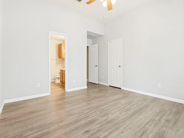 Large primary bedroom with laminated wood floors leading to ensuite bathroom