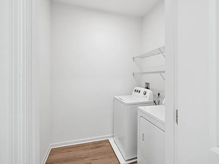 Modern laundry room with sleek washer and dryer, featuring elegant wooden flooring and ample shelving space.