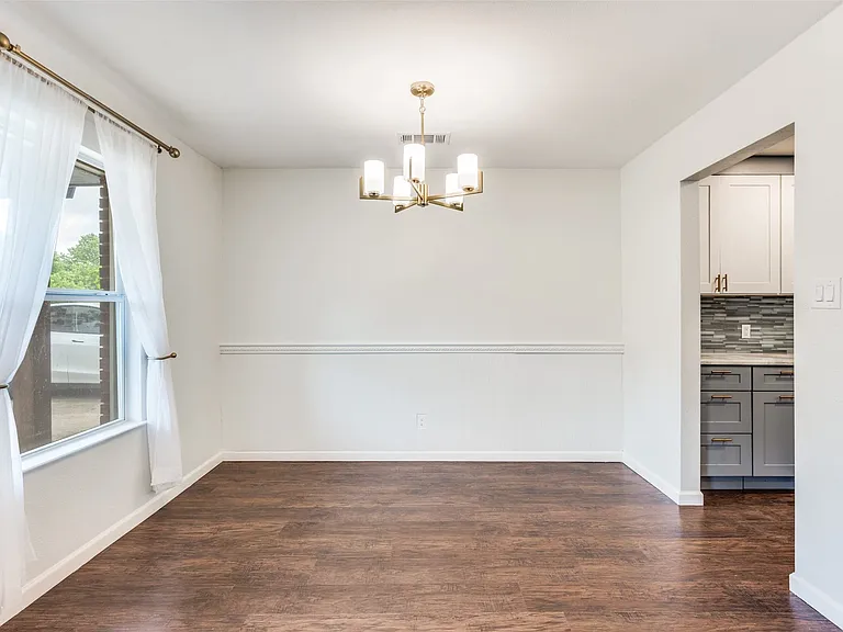 Spacious room featuring wood-finish flooring, white walls, and a contemporary chandelier