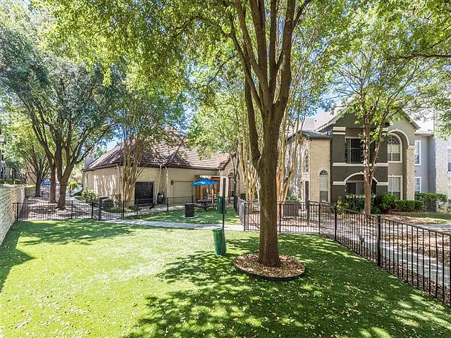 Fenced in dog park with lush landscape and shade trees located inside a courtyard