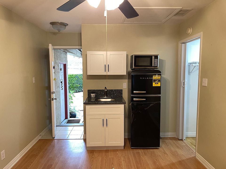 Large room with ceiling fan, sink and cabinets, refrigerator and microwave.