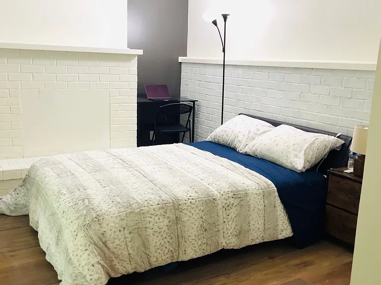 Furnished bedroom with a full-size bed, nightstand, and dedicated desk area, plus durable wood-look flooring.