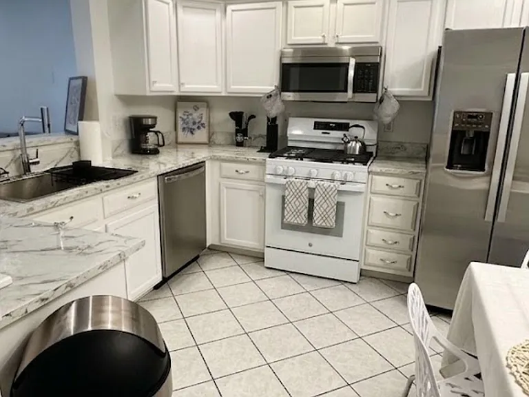 Well-equipped kitchen with ample white cabinetry, stone-look counters, and stainless appliances plus adjacent dining area.