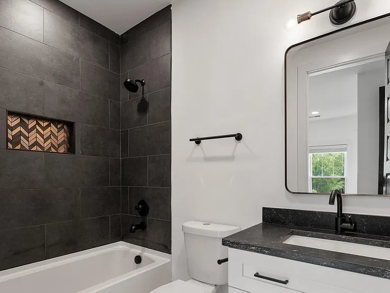 Updated bath with a tiled tub/shower, black fixtures, and a vanity with countertop sink and framed mirror.