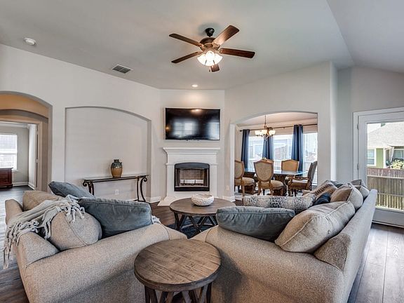 Vaulted ceiling with a ceiling fan, fireplace with a white mantel, arched doorways, wood-finish flooring, and a glass-paneled exterior door