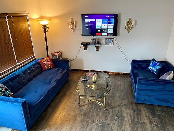 Living room featuring a large, blue velvet sofa and love seat. Along with a DVD player and smart TV.