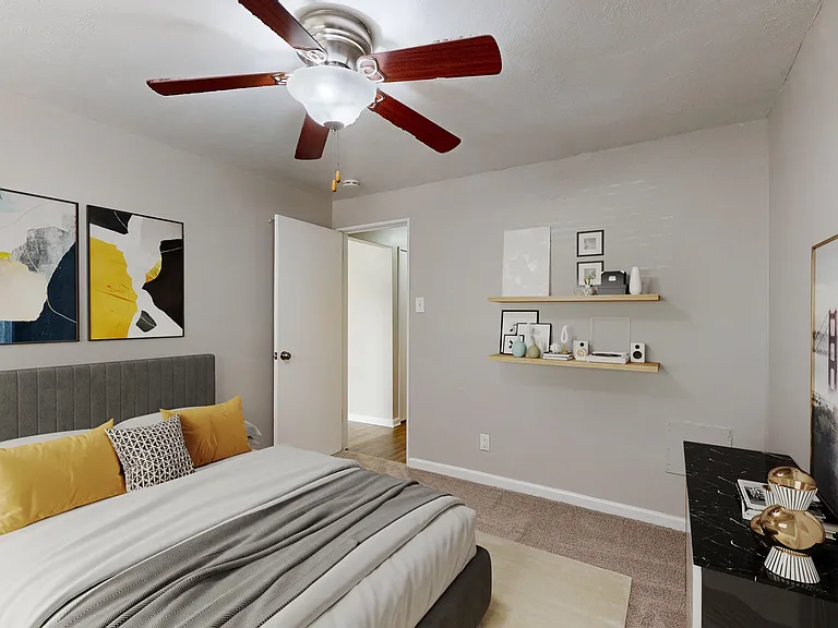 Inviting bedroom with contemporary decor, featuring a stylish queen bed with yellow accents, modern ceiling fan, and elegant artwork on the walls.