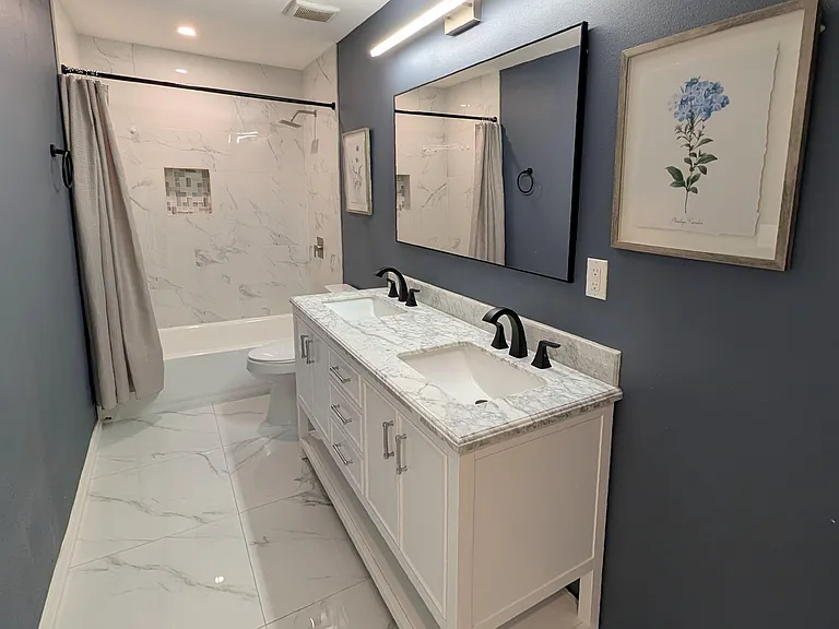 Updated bathroom with double-sink vanity, marble-look countertops, and a tiled tub/shower with built-in niche.
