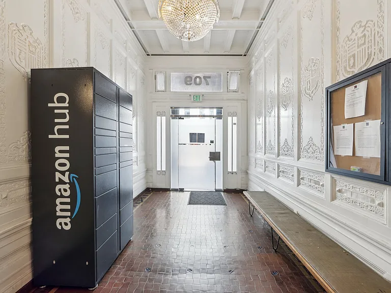 Ornate hallway with Amazon Hub locker, chandelier, bulletin board, wooden bench, and glass door