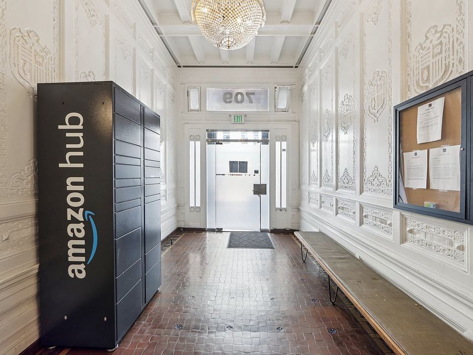 Ornate hallway with Amazon Hub locker, chandelier, bulletin board, wooden bench, and glass door