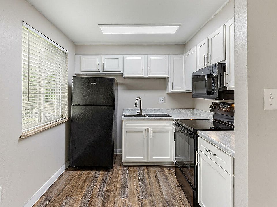 Modern kitchen with elegant white cabinetry, sleek black appliances, and spacious countertops, highlighted by natural light from a large window, creating a bright and inviting space.