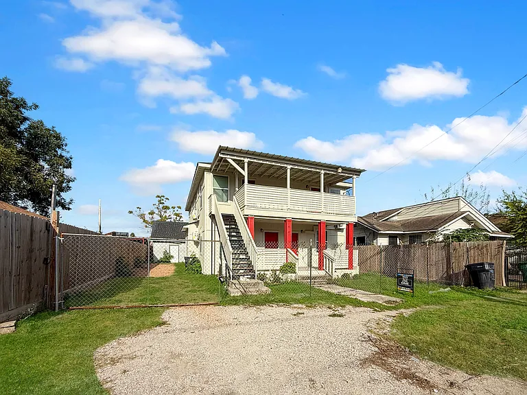This inviting two-story four-plex, featuring a spacious porch and vibrant red accents, offers a welcoming atmosphere and the promise of unobstructed views with the removal of the chainlink fence upon occupancy.