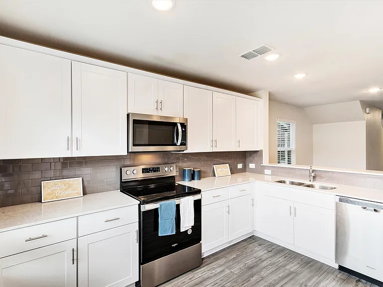 Kitchen featuring white cabinetry, stainless steel appliances including a microwave, oven/range, and dishwasher, light-toned countertops, and a gray subway tile backsplash
