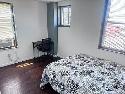 Bedroom offers a full bed setup plus a dedicated desk area, with two windows and wood-style flooring for easy upkeep.