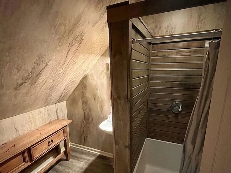 Private en-suite bathroom attached to one of the upstairs bedrooms, featuring a full shower and rustic wood detailing.