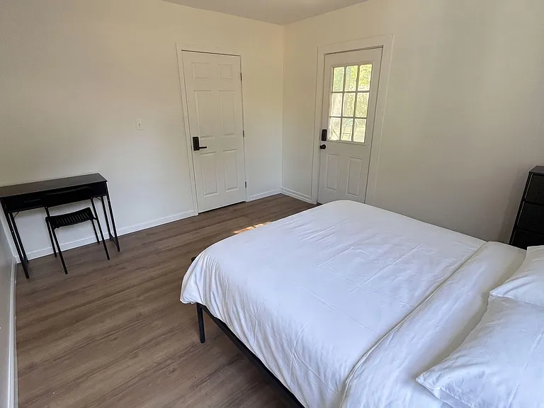 Spacious bedroom with wood-look floors, a work desk, and a private exterior door for convenient access.