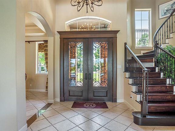 A large tiled foyer with a custom wrought iron chandelier, arched doorways lead to an elegant formal dining room and an elegant stairway with wood tread and wrought iron spindles.