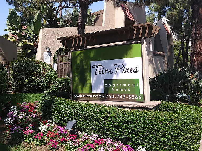 Enterance monument sign surrounded by beautiful gardens at Teton Pines Apartments in Escondido, California.