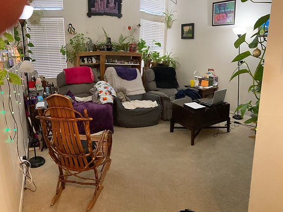 crowded living room with past tenants furniture, three recliners with shelving unit behind them much larger than appears