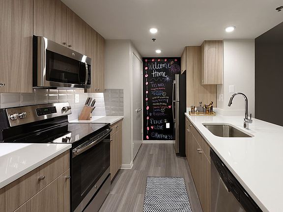 Renovated Package II kitchen with white quartz countertops, white tile backsplash, driftwood cabinetry, stainless steel appliances, and hard surface plank flooring