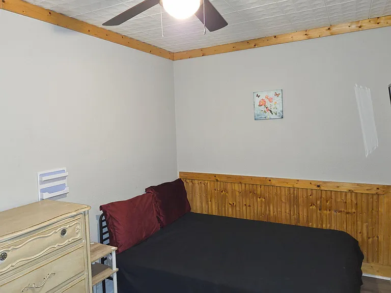 Private bedroom with a furnished bed, ceiling fan, and wood wainscoting for a warm, practical setup.