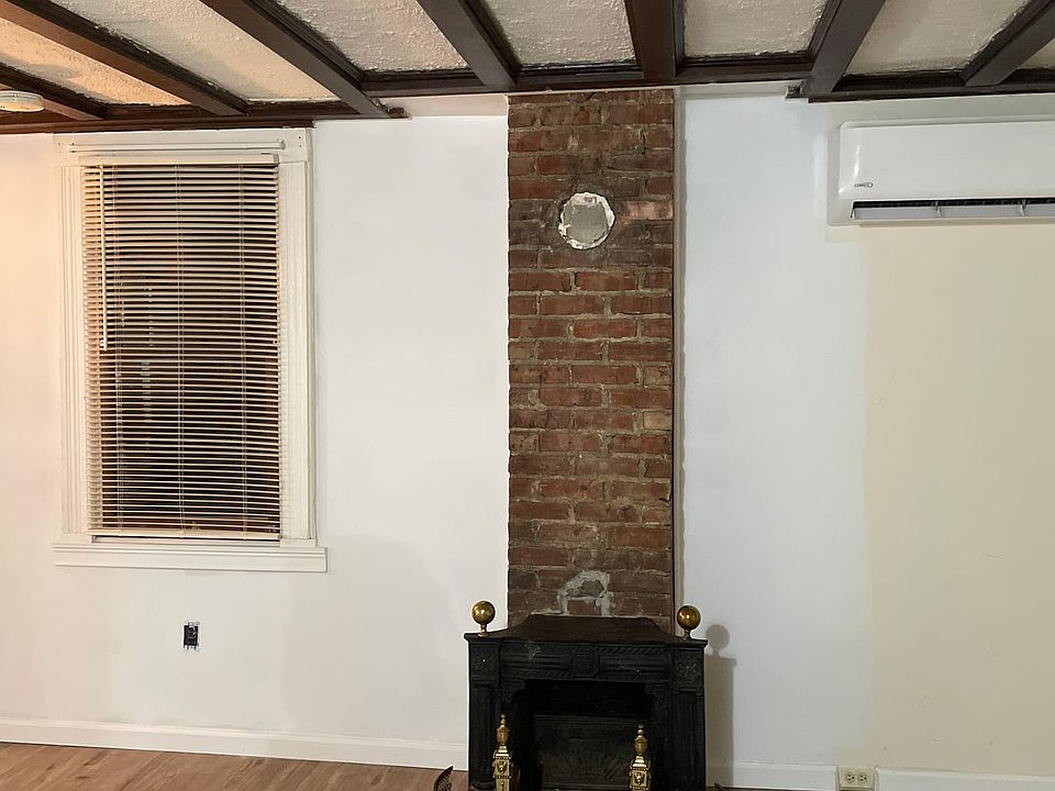 Large living room with new flooring, exposed brick, decorative fireplace, and ornate wood coffered ceiling with loads of natural light