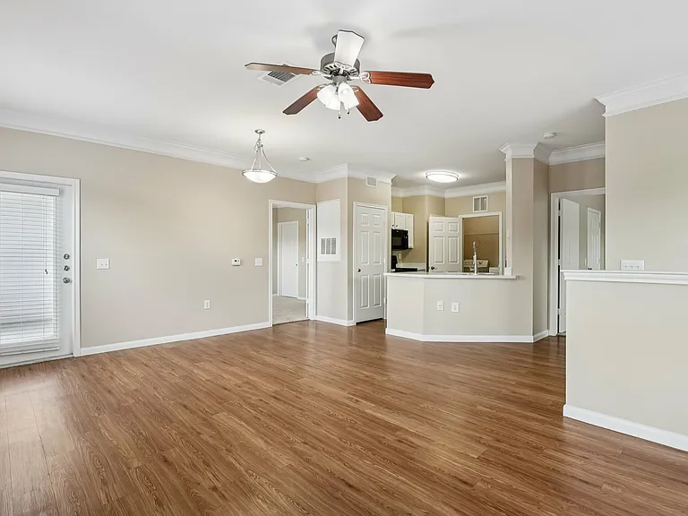 Spacious open-concept living room with elegant wood-style floors and modern recessed lighting, leading to a bright kitchen with sleek cabinetry and a stylish ceiling fan. Spacious open-concept living room with elegant wood-style floors and modern recessed