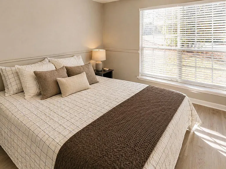 Well-sized bedroom with a full bed setup, side tables, and a large window with blinds for comfortable natural light.