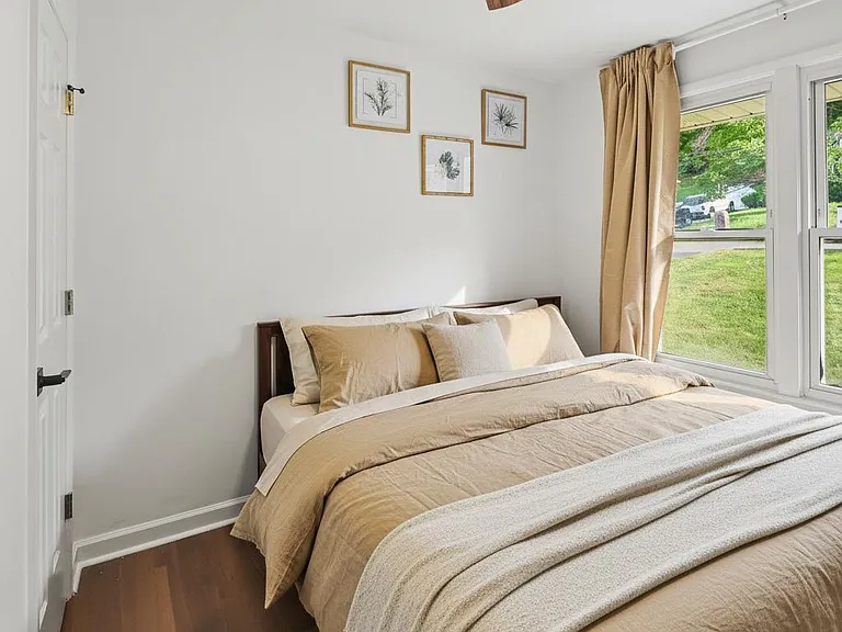 Comfortable bedroom with a king bed, ceiling fan, and a large window with curtains overlooking the yard.