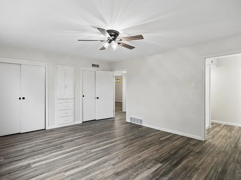 Spacious room featuring wood-finish flooring, a ceiling fan with integrated lighting, built-in cabinetry with drawers, and multiple closet systems