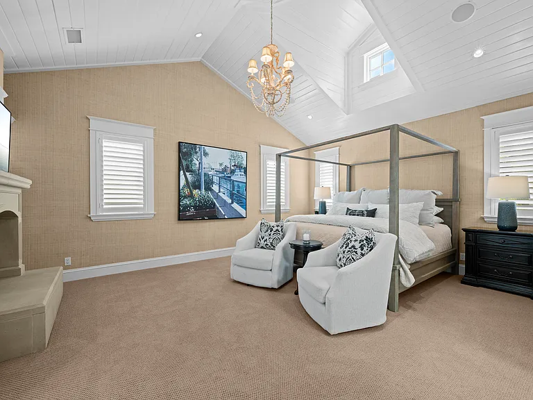 Primary Bedroom with wood vaulted ceilings, grass cloth wallpaper, shutters and fireplace.