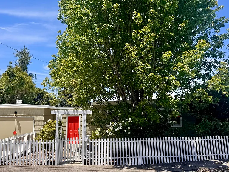This 1952 bungalow has striking curb appeal with mature trees, private fenced frontage, and a welcoming architectural entry anchored by a striking red front door.