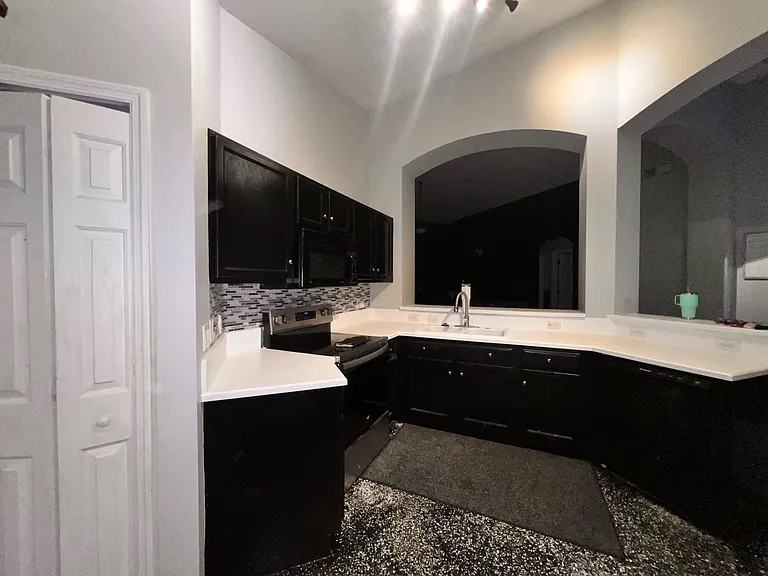 Updated kitchen with dark cabinetry, solid-surface counters, mosaic backsplash, and a breakfast bar overlooking the living ar