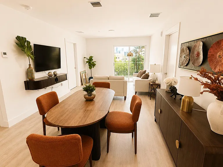 Open-concept dining and living area with a full dining set, wall-mounted TV, and sliding doors to a balcony.